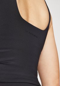 Czarny sportowy top na ramiączkach o dopasowanym kroju, wykonany z elastycznego materiału, z delikatnym wytłoczonym logo "GIRLFRIEND" na boku.