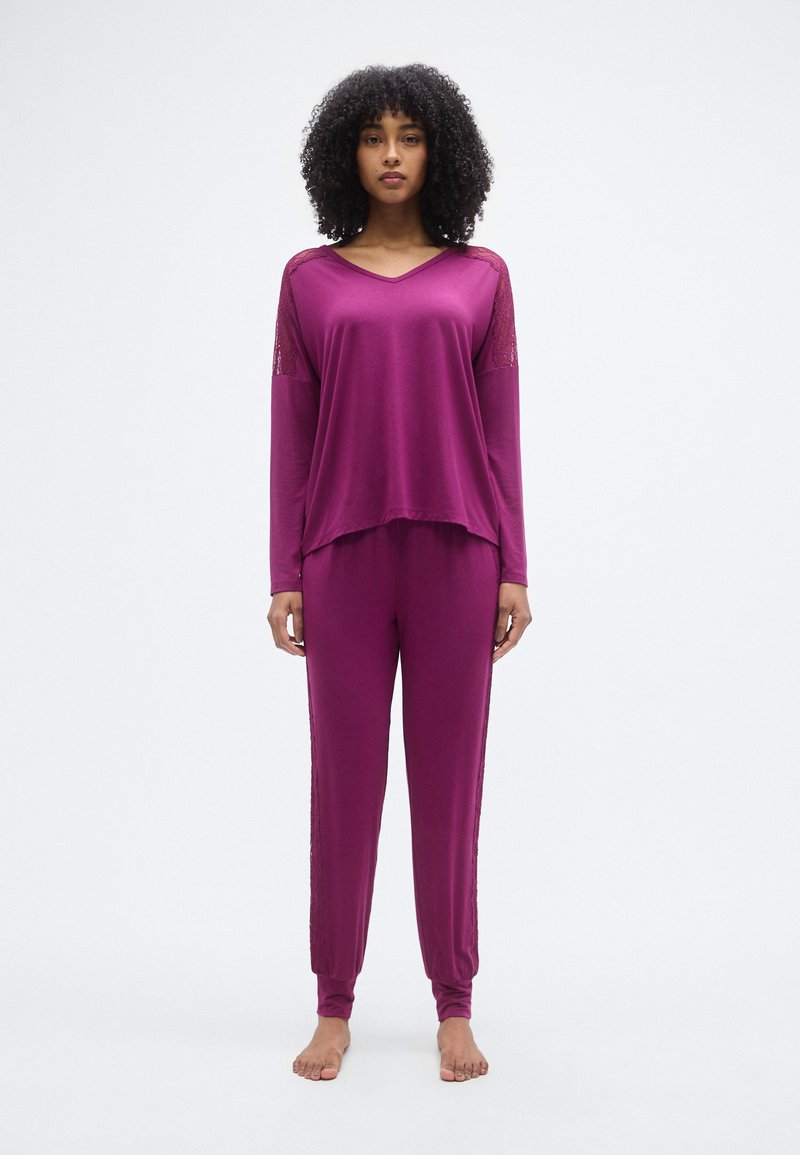 Μωβ σετ σαλονιού με μπλούζα μακρυμάνικη και V-λούκο με λεπτομέρειες δαντέλας και παντελόνι με κωνικό κόψιμο, κατασκευασμένο από απαλό, ελαφρύ υλικό.