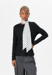 Black long-sleeve shirt paired with a white polka dot scarf. The scarf features a sleek design with a smooth texture and pointed ends.