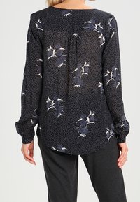Blusa a maniche lunghe in tessuto blu navy con pois bianchi e motivo floreale. Presenta un collo rotondo e una vestibilità ampia. Tessuto leggero e semi-trasparente.
