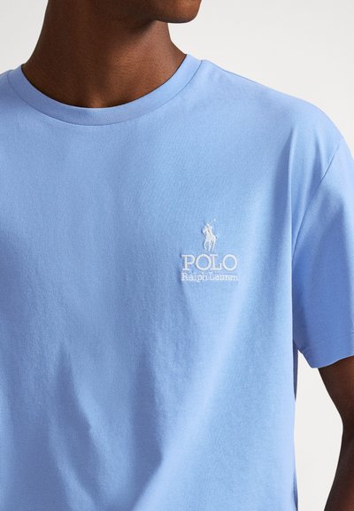 Ανοιχτό μπλε βαμβακερό μπλουζάκι με στρογγυλή λαιμόκοψη, με λευκό κεντημένο λογότυπο παίκτη πόλο στο αριστερό στήθος. Μαλακή υφή, άνετη εφαρμογή.