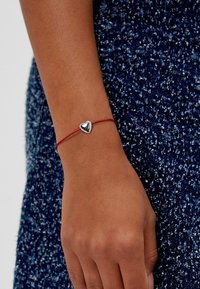 Rotes Armband aus Schnur mit einem polierten Silberschmuckherz, glatter Textur und minimalistischem Design, geeignet für die Freizeit.