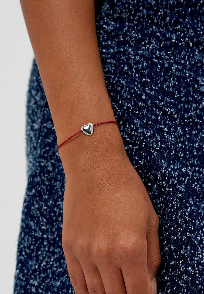 Rotes Armband aus Schnur mit einem polierten Silberschmuckherz, glatter Textur und minimalistischem Design, geeignet für die Freizeit.