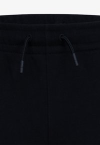 Černé bavlněné tepláky s elastickým pasem a šňůrkou na stažení, hladkým povrchem a plochým švem po stranách.