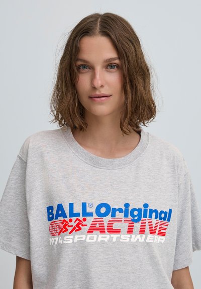 Pelēka kokvilnas T-krekls ar sarkano un zilo tekstu: "BALL Original ACTIVE SPORTSWEAR 1974." Vienkāršs dizains un brīvs piegriezums ar īsām piedurknēm.