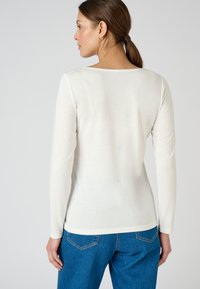 Langarm T-shirt met ronde hals in off-white, gemaakt van een zachte stof. Gecombineerd met blauwe denimbroek, met een relaxte pasvorm en taille naaddetail.