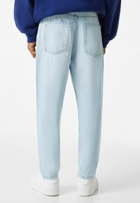 Ljusblå denimjeans med en avslappnad passform, som har två bakfickor och en avsmalnande bendesign. Matchas med vita sneakers.