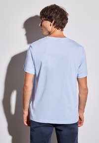 T-shirt en coton bleu clair avec un col rond et des manches courtes, présenté de dos. Texture lisse, design minimal, bords nets.