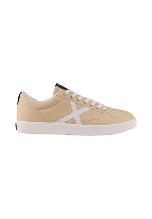 Zapatilla de lona beige de corte bajo con cordones blancos, suela blanca y un gran "X" blanco en el lateral.