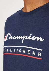 Navy blue cotton t-shirt featuring white and red "Champion ATHLETICWEAR" graphic print on the front. Short sleeves and round neckline.