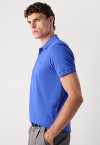 Camisa polo azul feita de tecido suave, com colarinho clássico, mangas curtas e um logótipo discreto no lado esquerdo do peito.