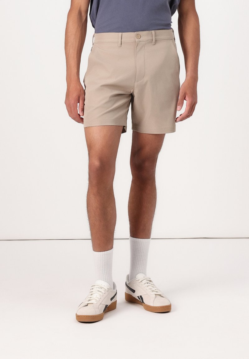 Beige shorts med flad front, to sidelommer og knaplukning. Båret med hvide ankelstrømper og cremefarvede sneakers med sorte detaljer.