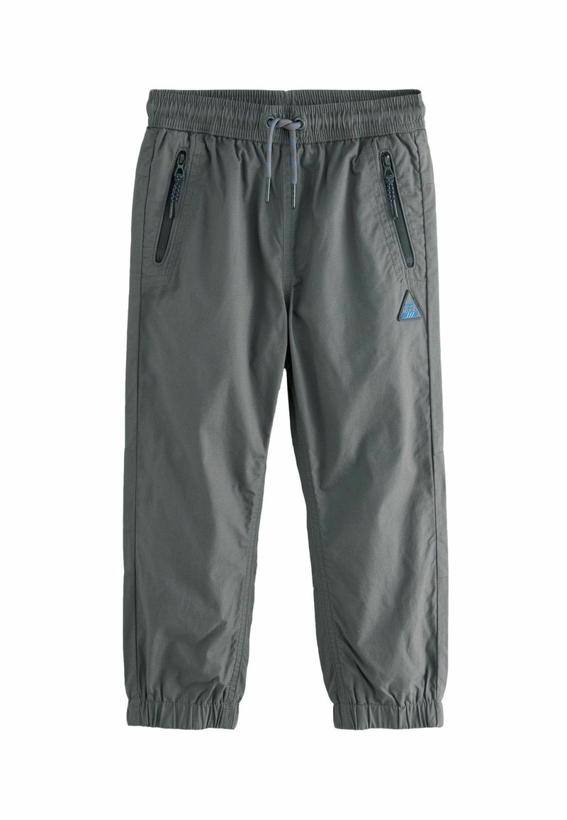 Pantalon de sport gris avec taille élastique, cordon de serrage réglable et deux poches latérales zippées. Présente des poignets effilés et une étiquette avec logo.