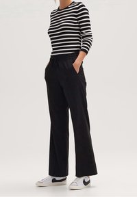 Czarne spodnie o szerokich nogawkach z elastycznym paskiem w talii i bocznymi kieszeniami, zestawione z czarno-białą, prążkowaną bluzką z długim rękawem w paski oraz białymi trampkami.
