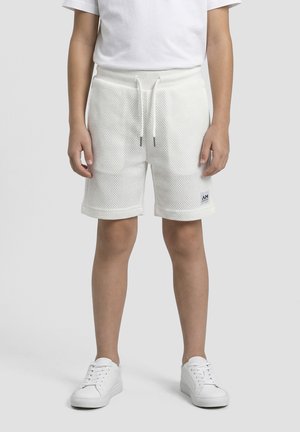 Kind draagt witte gestructureerde shorts met aantrekkoord, wit T-shirt en witte sneakers, staand tegen een effen grijze achtergrond.
