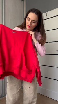 Piros Nike pulóver, kerek nyakkal, hosszú ujjakkal és elülső zsebbel. A mellkasán egy kis fehér logó található, és laza szabású dizájn jellemzi.