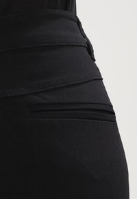 Schwarzer Rock mit glatter Textur, der über einen strukturierten Taillenbund und zwei horizontale Nahtdetails in Hüfthöhe verfügt.