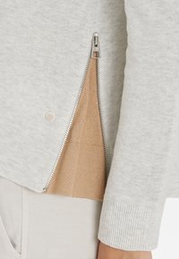 Maglione grigio chiaro con chiusura a zip laterale, con fodera beige. Polsini e orlo a costine, realizzato in tessuto morbido e testurizzato.