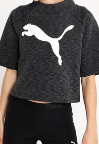 Czarna, krótka koszulka sportowa z teksturowanym wykończeniem i szerokimi rękawami, z wyraźnym białym logo Pumy z przodu.