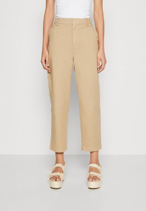 Beige katoenen wijde broek met voorzakken, een vlakke taille en een iets verkorte lengte, gecombineerd met lichte, gespannen platformsandalen.