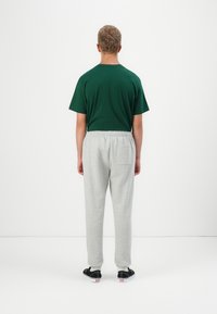 Grønn bomull t-skjorte og lysegrå joggebukser. Løs passform med elastisk linning og sidelomme. Svarte sko med hvite detaljer.