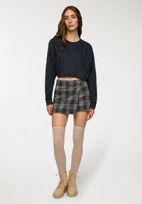 Maglione corto a maglia navy con motivo testurizzato, abbinato a una mini gonna a scacchi. Calze beige fino al ginocchio e stivaletti color tan con lacci completano l'outfit.