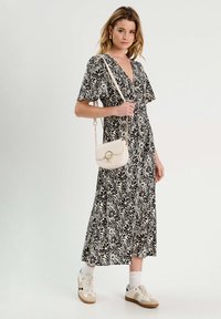 Robe florale noire et crème avec des manches courtes et un col en V, accompagnée d'un petit sac à main blanc et de baskets beiges avec des chaussettes blanches.