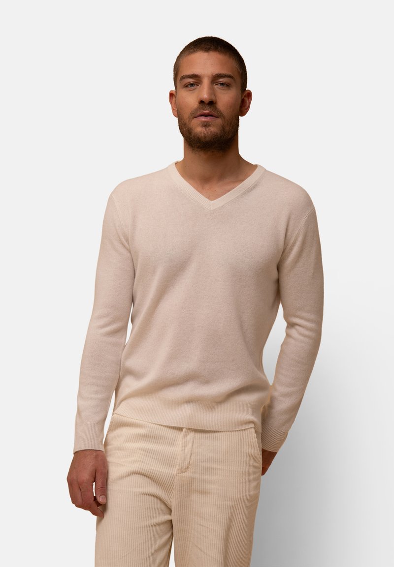 Světle béžový svetr s výstřihem do V a dlouhými rukávy, měkká textura, přiléhavý design, kombinovaný s žebrovanými béžovými kalhotami. Jednoduchá a neutrální paleta barev.