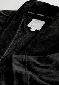 Schwarzer, strukturierter Stoffmantel mit Kragen und weiten Ärmeln. Das Etikett innen lautet "NEXT time to dream." Weiches, plüschiges Material.