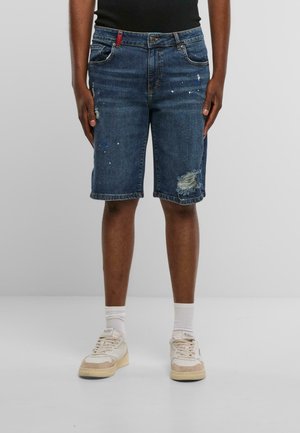 Dunkelblaue Denim-Shorts mit distressed Details, die Farbkleckse, einen fransigen Saum und ein klassisches Fünf-Taschen-Design aufweisen.