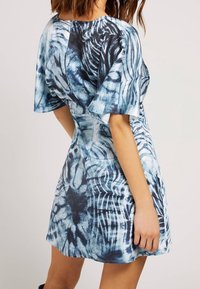 Robe courte bleue et blanche avec des motifs abstraits, une coupe décontractée et des manches fluides. Le tissu semble léger et texturé.