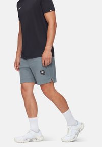 Mäns idrottskläder med en svart kortärmad tröja och ljusgrå shorts med en logotypapplikation, kompletterat med vita strumpor och grå löparskor.
