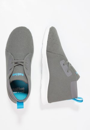 Een paar grijze casual veterschoenen met witte zolen en een blauwe binnenvoering en hieltreklusjes, gepositioneerd in bovenaanzicht en zijaanzicht op een witte achtergrond.