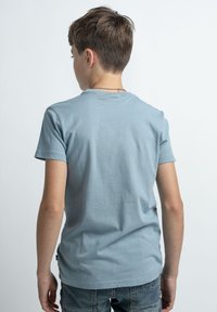 Camiseta de algodón azul claro con mangas cortas, un cuello redondo y una textura suave. La vista muestra la parte posterior con un detalle mínimo.