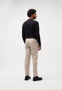 Chemise noire à manches longues, pantalon beige côtelé et bottines noires. Design minimaliste, coupe ajustée, poches arrière visibles sur le pantalon.