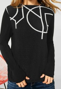 Svart långärmad skjorta med vitt abstrakt geometriskt mönster. Har rund halsringning och något utställda ärmar. Slät textur.