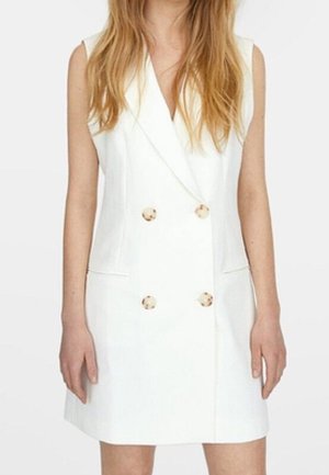 Mouwloze witte double-breasted blazerjurk met vier knopen en twee zakken aan de voorkant, gedragen door een persoon met lang haar.