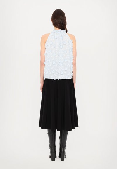 Svetlo modra brezrokavna majica z teksturiranimi cvetličnimi okraski, v kombinaciji z črno midi krilo in sijočimi črnimi visokimi škornji.