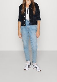 Černá sametová zkrácená bunda, bílý tílko, světle modré džíny s vysokým pasem a bílé tenisky s červenými a černými akcenty.