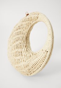 Woven straw bag with a circular cutout design, cream color, textured surface, and a small leather accent at the top for easy carrying.