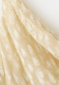 Tissu beige clair avec une texture douce et transparente, et des motifs floraux en relief créant un design subtil et élégant.