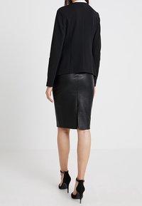 Svart skräddarsydd kavaj med en strukturerad design, kombinerad med en elegant svart läder blyertskjol med en slits bak. Svarta klackar fulländar looken.