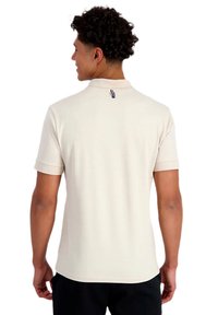 Polo shirt color beige claro en algodón suave, con mangas cortas, un cuello clásico y un pequeño logo en la parte posterior del cuello.