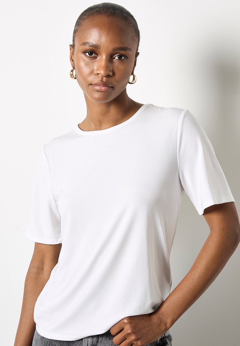 Hvid kortærmet T-shirt lavet af glat stof med en rund udskæring og afslappet pasform. Enkelt design uden synlige mønstre eller hardware.