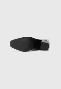 Zwarte rubberen outsole met een gemarmerd grippatroon, overgaand naar een bruin bovenste gedeelte met een gladde afwerking. Open teenontwerp.