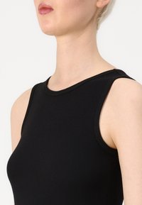 Μαύρο ριμπ αμάνικο τοπ με στρογγυλή λαιμόκοψη και λεία υφή, σχεδιασμένο για εφαρμοστή σιλουέτα.