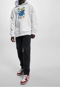 Sweat à capuche blanc avec un motif graphique bleu et le texte "fly high", assorti à un jean noir et des baskets rouges et blanches avec un design en forme de swoosh.