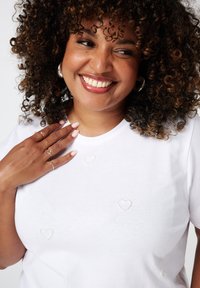 Witte T-shirt van zachte katoen, met delicate hartvormige kraalversieringen. Ronde halslijn en korte mouwen.