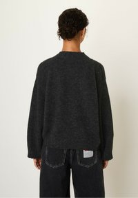 Dark gray knit sweater with a round neckline and dropped shoulders, paired with loose black jeans featuring a label on the back pocket.