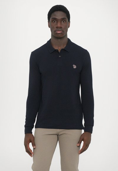 Polo de manga longa azul-marinho com colarinho clássico, apresentando um pequeno logótipo bordado no lado esquerdo do peito e punhos canelados.